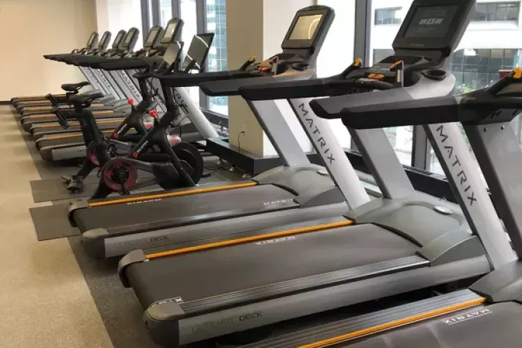 Modern fitness center at 1818 Market featuring a row of Matrix treadmills and stationary bikes lined up beside large windows with city views, offering a bright and energizing workout space.