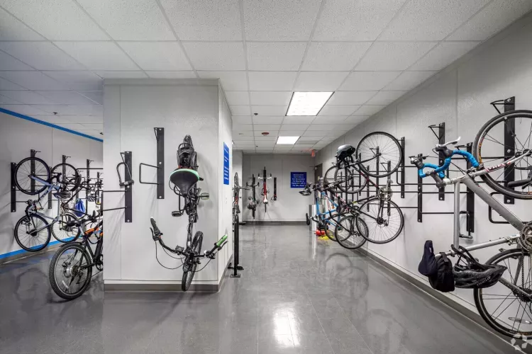 Secure indoor bike storage room at 1818 Market, featuring vertical wall-mounted racks holding multiple bicycles in a clean, well-lit space with polished floors and a suspended ceiling.